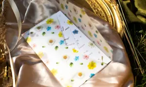 Otwarta koperta z zaproszeniem na ślub ozdobiona akwarelowymi kwiatami, leżąca na satynowej tkaninie.