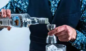 Barman nalewa wódkę Żubrówka Biała z butelki do miarki barmańskiej nad szklankę z lodem.
