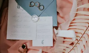 Eleganckie zaproszenia ślubne, obrączki i ozdobne liście na różowym tle.