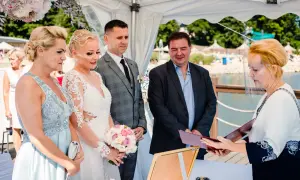 Para ślubna, świadkowie i urzędniczka z przyłbicą podczas ceremonii ślubnej nad jeziorem.