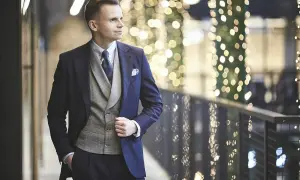 Elegancki mężczyzna w granatowym garniturze i kamizelce, gotowy na wieczór w stylu cocktail attire, na tle migoczących świateł.