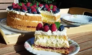 Prosty tort biszkoptowy z kremem i owocami leśnymi, udekorowany malinami i borówkami.