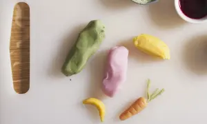 Kolorowe masy cukrowe uformowane w marchewkę, banana i inne kształty na białej desce.