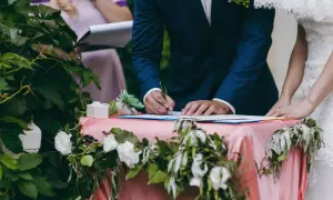 Pan młody podpisuje dokumenty ślubne przy udekorowanym stole.
