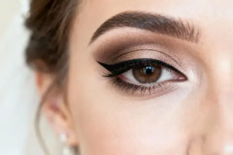 Oko kobiety z subtelnym makijażem ślubnym naturalnym. Brązowe cienie, kreska eyelinerem i podkreślone brwi.