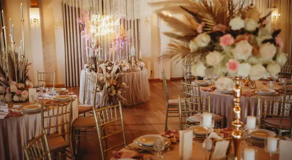 Elegancka sala weselna z neonem "All you need is love". Złote krzesła, pudrowo-różowe obrusy i bujne kwiaty. Zastanawiasz się, ile kosztuje dekoracja sali weselnej?
