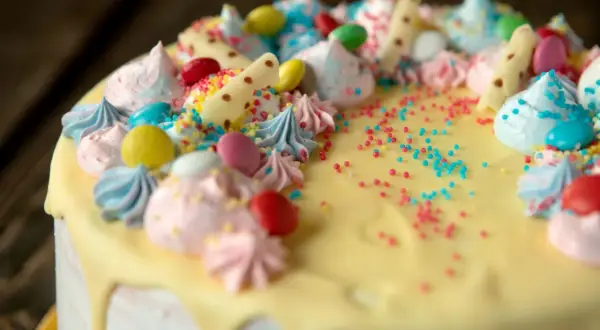 Kolorowy tort z kremem, bezą, cukierkami i posypką.