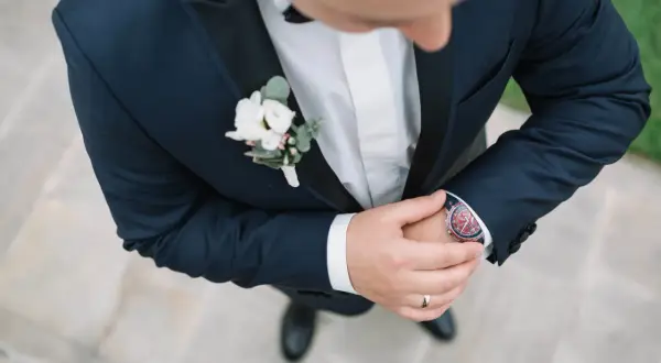 Elegancka butonierka dla pana młodego i świadka, ozdobiona białymi kwiatami i zielonymi liśćmi, dodaje szyku granatowemu garniturowi.