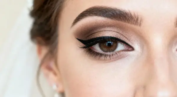 Oko kobiety z subtelnym makijażem ślubnym naturalnym. Brązowe cienie, kreska eyelinerem i podkreślone brwi.