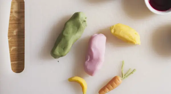 Kolorowe masy cukrowe uformowane w marchewkę, banana i inne kształty na białej desce.