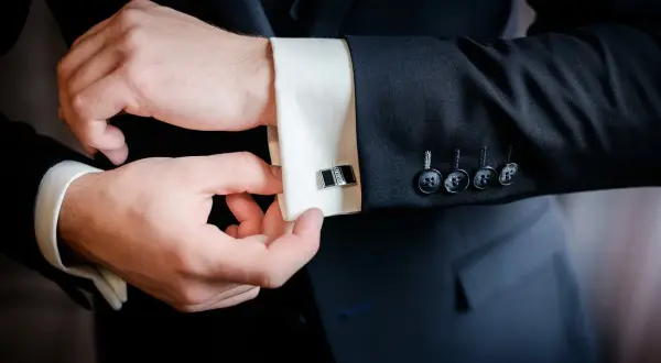 Mężczyzna zapina eleganckie spinki do mankietów koszuli, pokazując jak zapiąć spinki do koszuli.