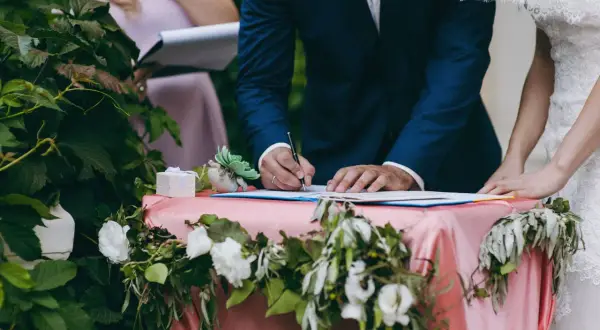 Pan młody podpisuje dokumenty ślubne przy udekorowanym stole.