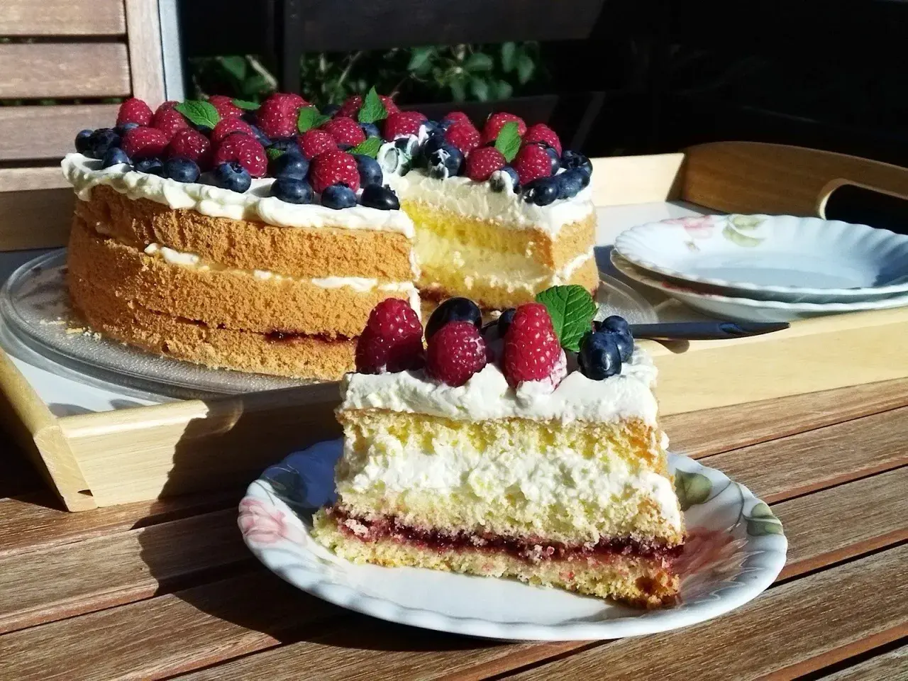 Prosty tort biszkoptowy z kremem i owocami leśnymi, udekorowany malinami i borówkami.