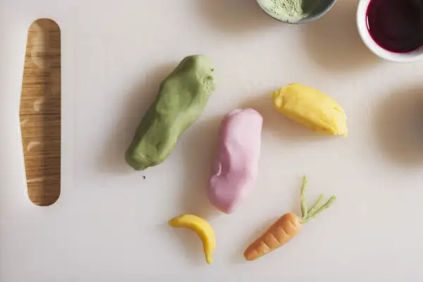 Kolorowe masy cukrowe uformowane w marchewkę, banana i inne kształty na białej desce.