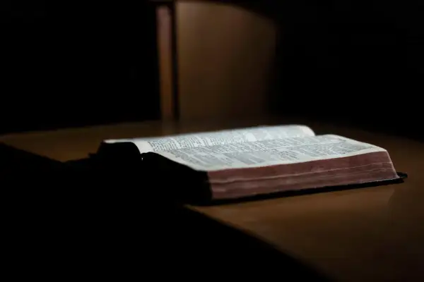 Otwarta Biblia leżąca na drewnianym stole, oświetlona od góry.
