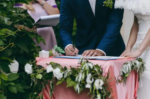 Pan młody podpisuje dokumenty ślubne przy udekorowanym stole.